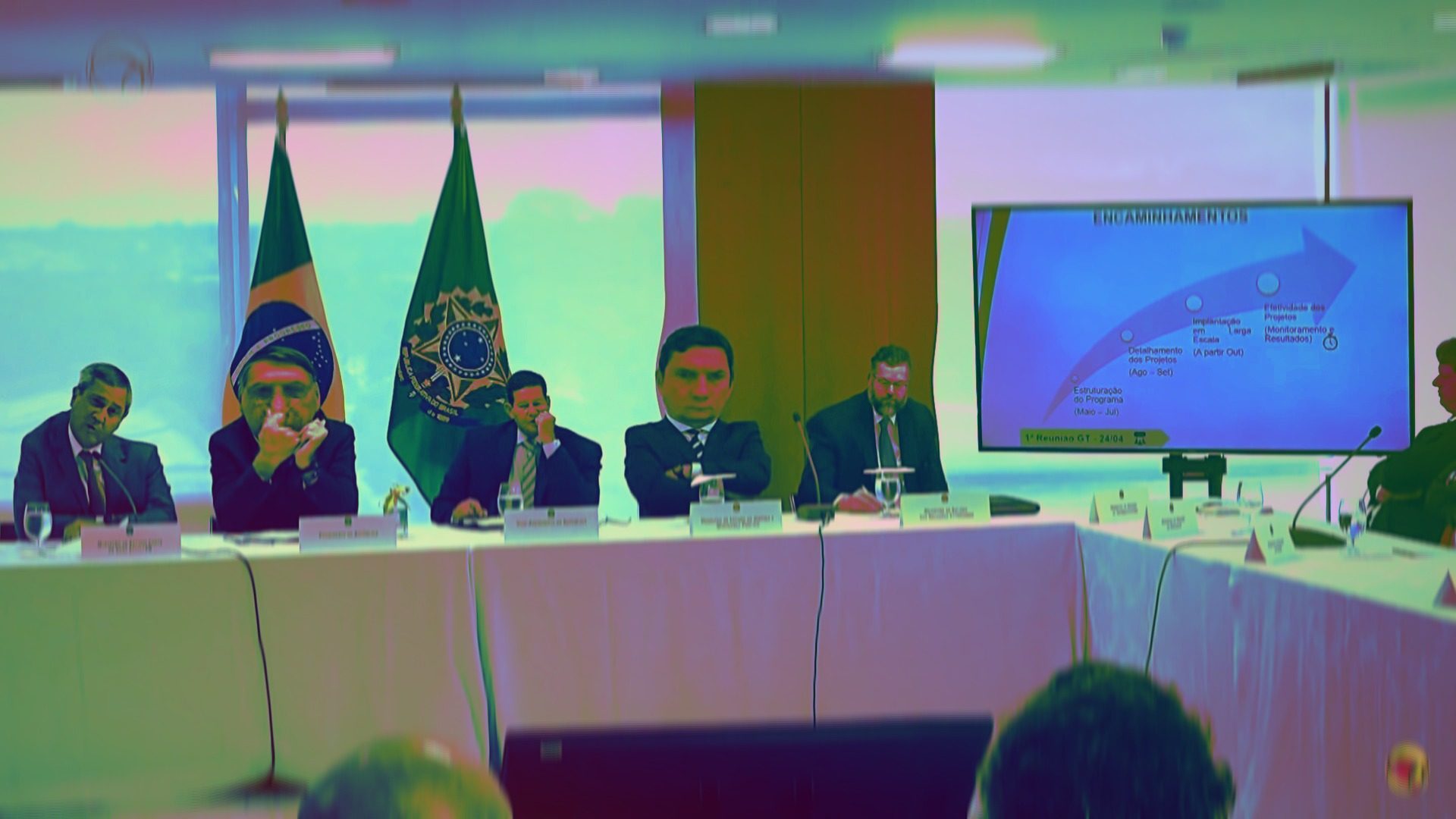 ministros e presidente bolsonaro sentados a mesa, com cores fortes e distorcidas